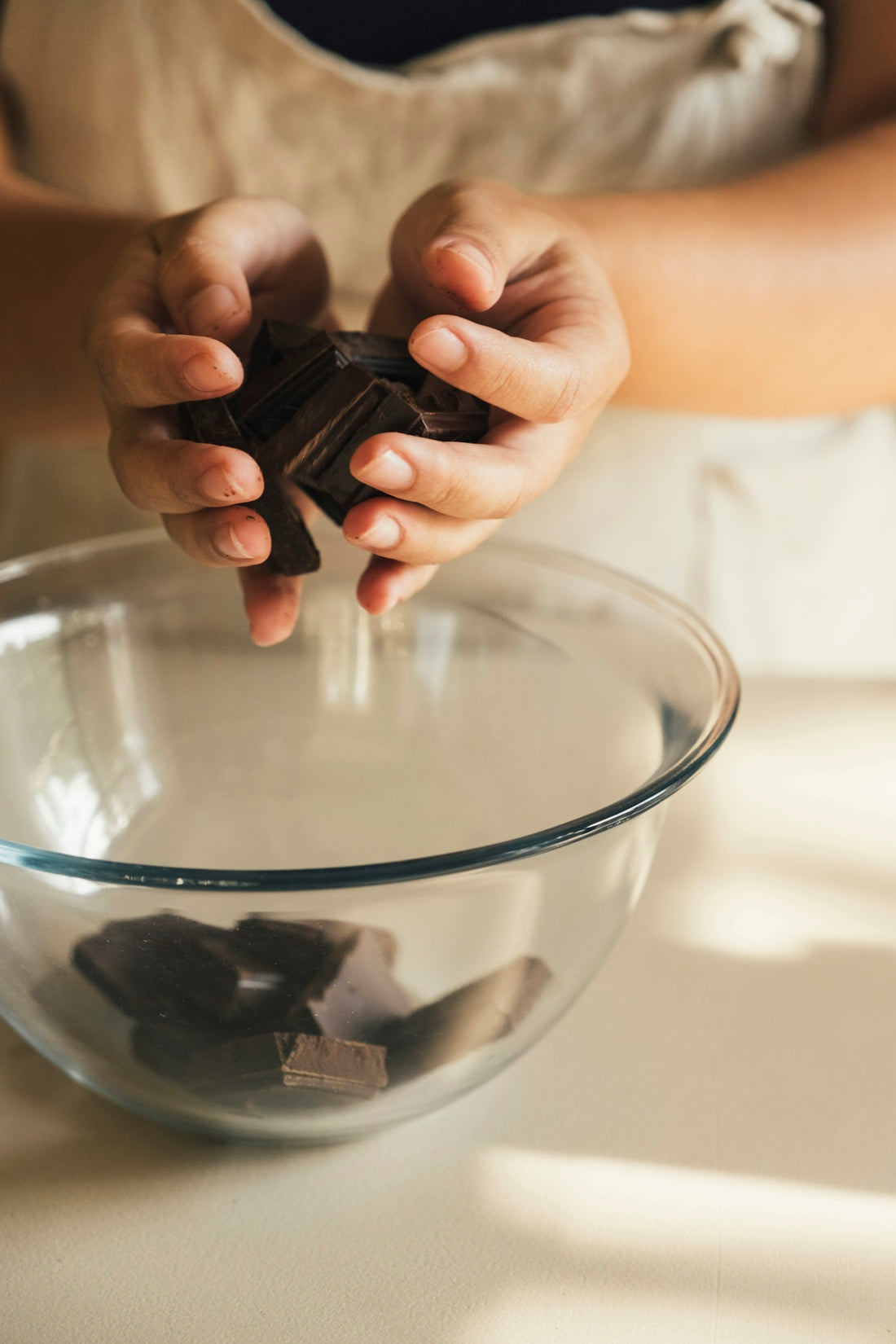 Hands adding chocolate chunks to a glass bowl
